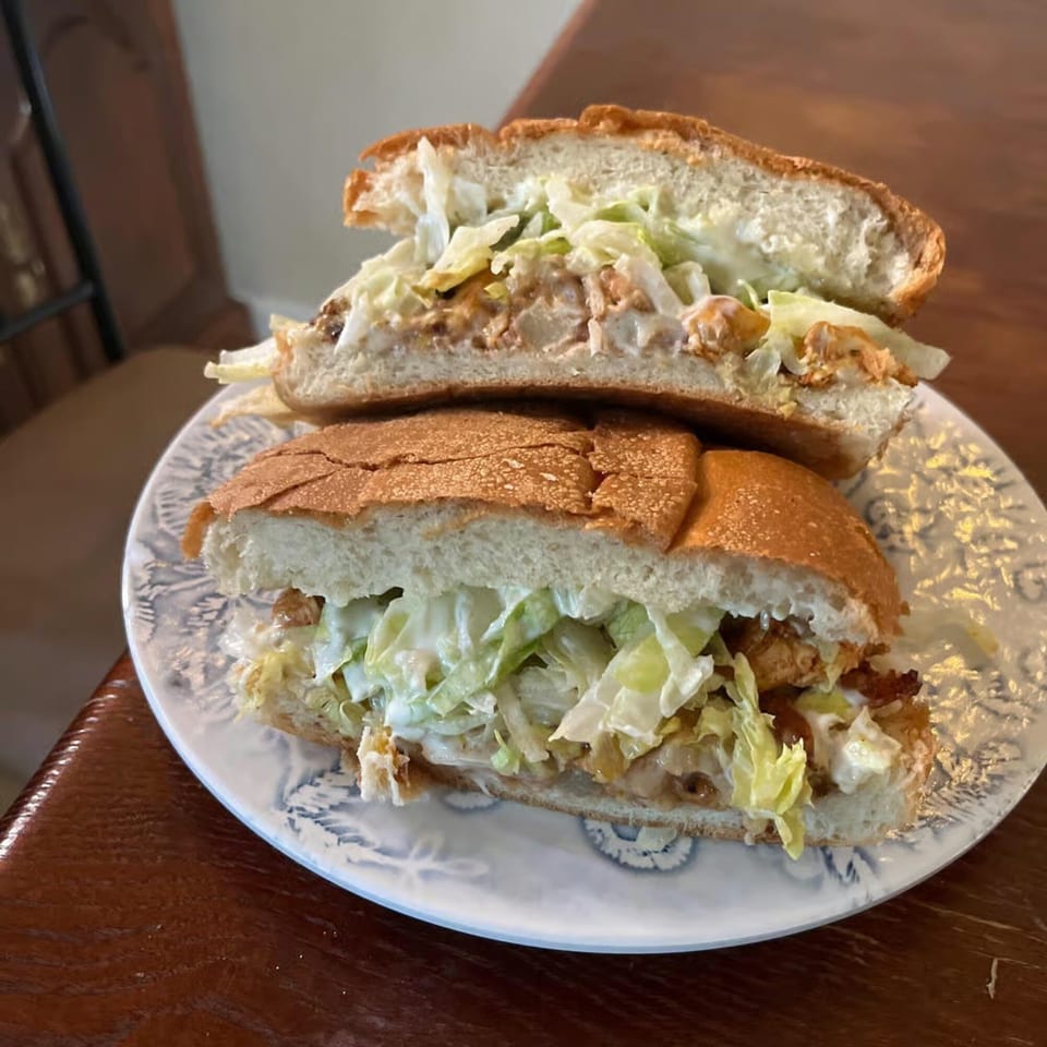 A large po'boy sandwich, cut in half, filled with fried shrimp, lettuce, and sauce.