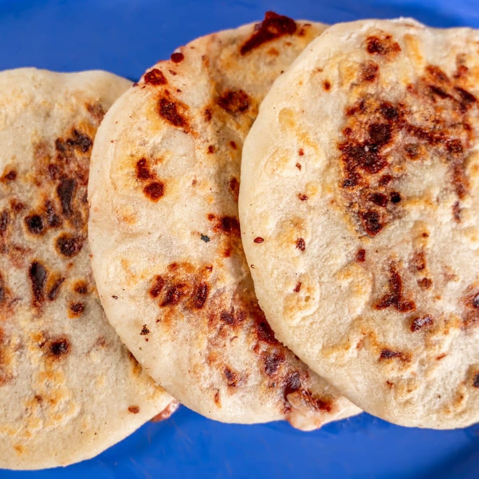 Three golden-brown pupusas with charred spots, arranged on a vibrant blue plate.