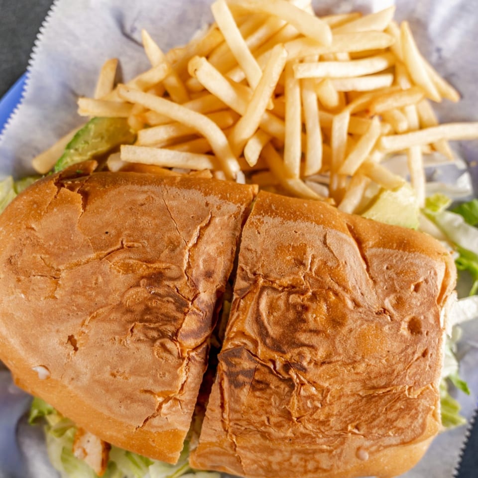A large sandwich cut in half, filled with lettuce and avocado, served with a side of french fries.