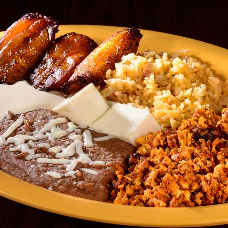 A yellow plate with fried plantains, rice, refried beans, cheese, and scrambled eggs.