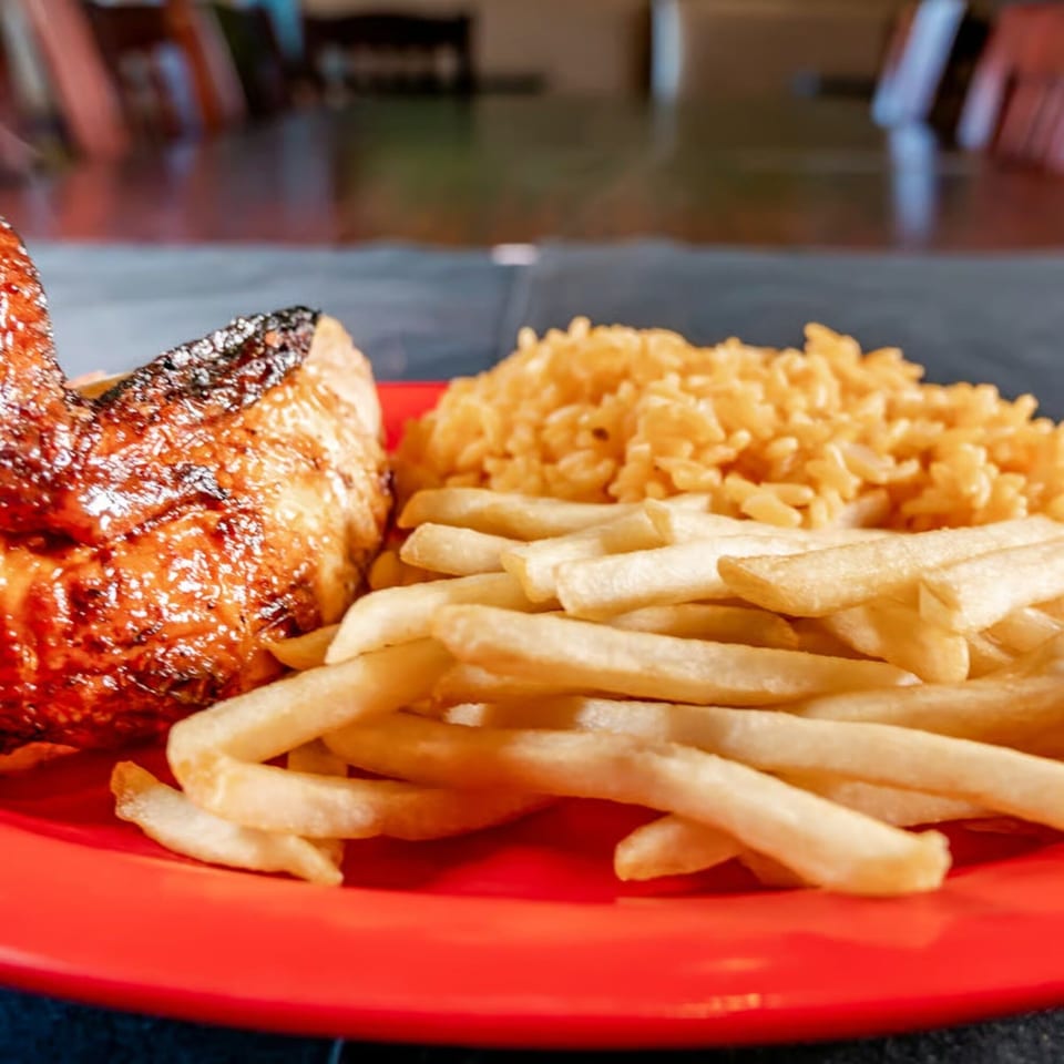 Grilled chicken leg quarter, golden fries, and yellow rice on a vibrant red plate.