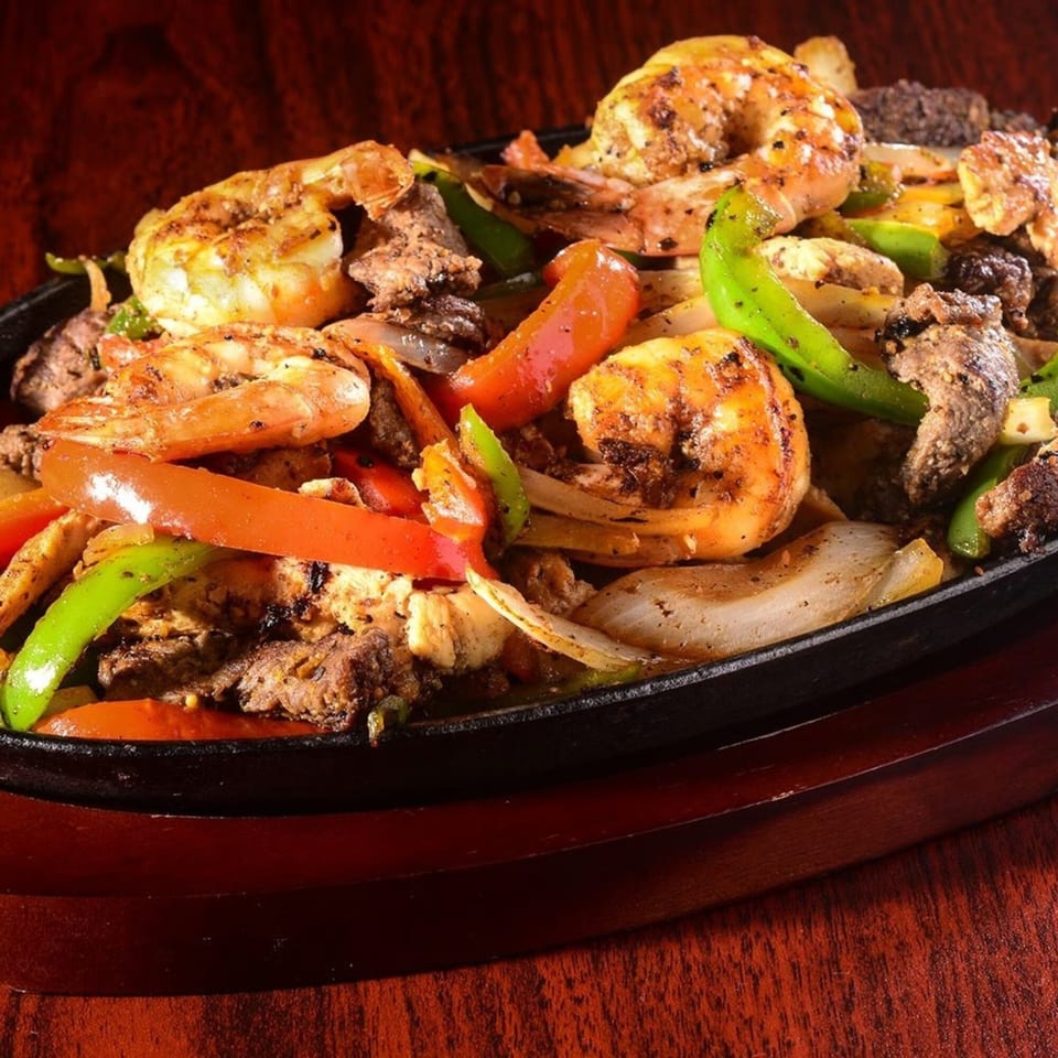 Sizzling fajitas with shrimp, beef, chicken, bell peppers, and onions in a cast iron skillet.